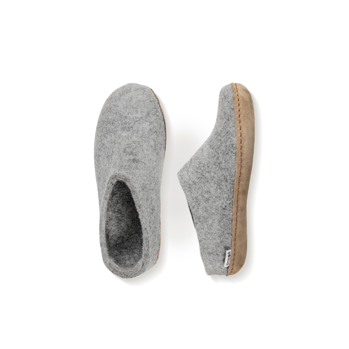 An overhead view of two light grey felted wool slippers. One is pictured straight on, showing the top face of the slipper, while the other lays on its side, showing the profile with tan leather sole with a row of stitching. 