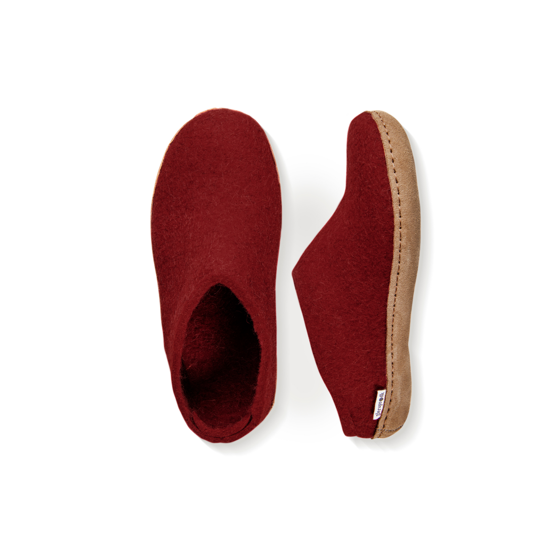An overhead view of two deep crimson felted wool slippers. One is pictured straight on, showing the top face of the slipper, while the other lays on its side, showing the profile with tan leather sole with a row of stitching.