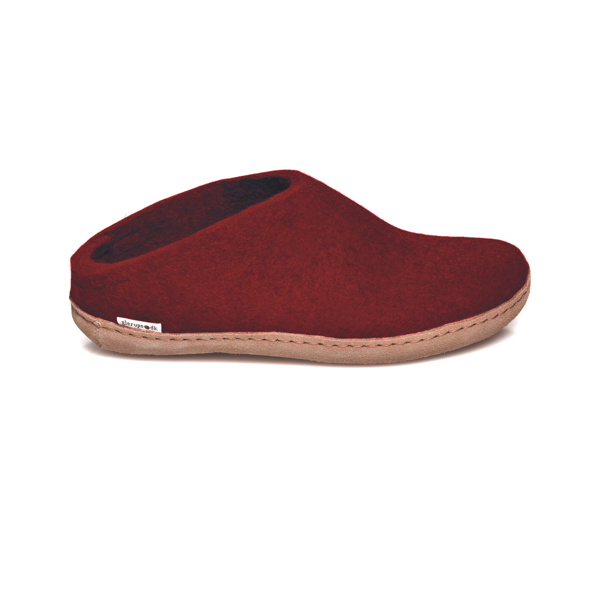 A deep crimson slipper is pictured in profile, showing the low back of the heel. The bottom lined in tan leather has a small tag with the brand name attached in the seam where the leather meets the felted wool.
