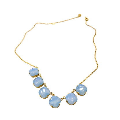 A top-down view of a necklace with a thin, unclasped gold chain and six light blue, translucent crystals.