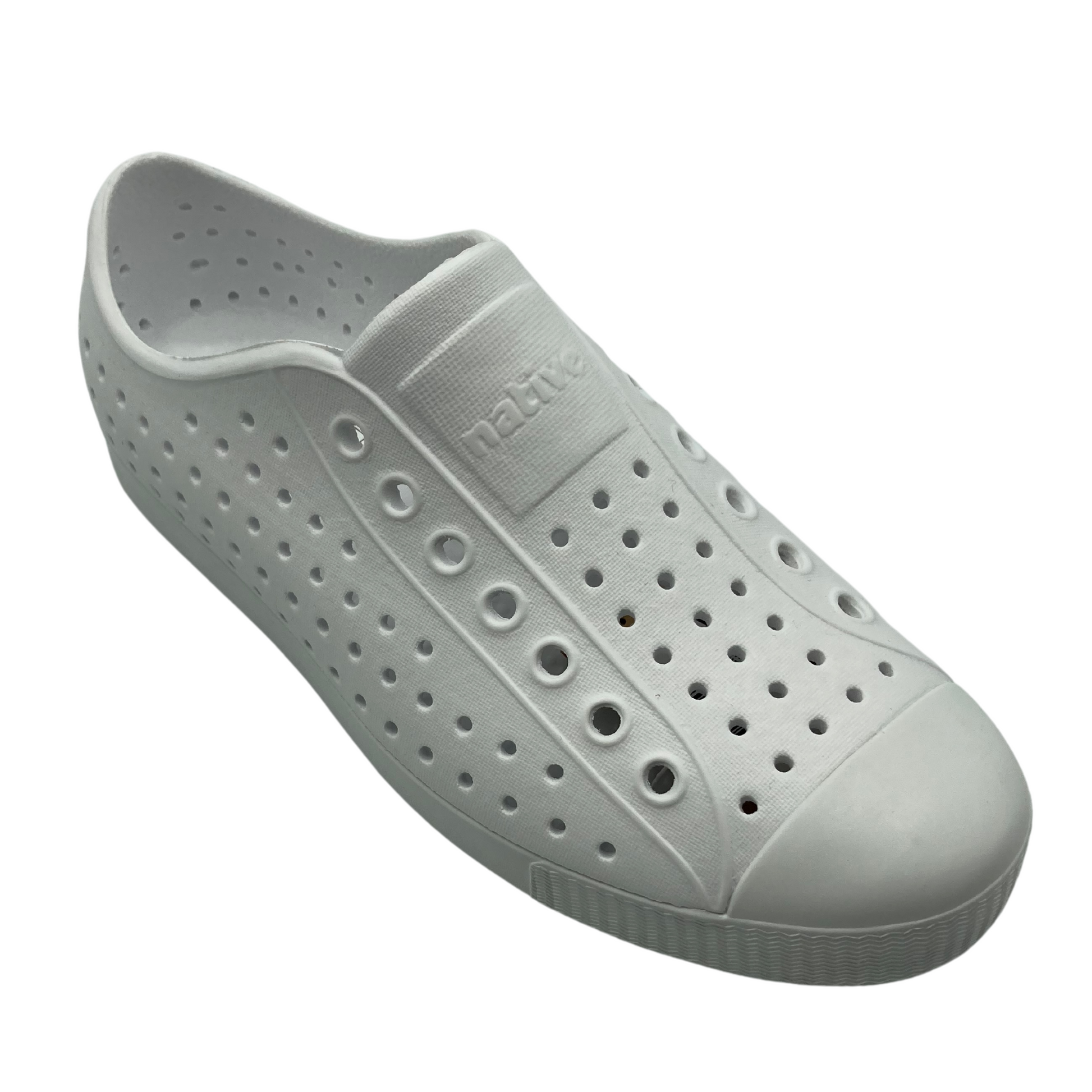 A plain white sneaker with larger perforations running parallel down the front, a plain toe box, and a square on the top front tongue reading "native" that is seemingly contoured into the form of the shoe.