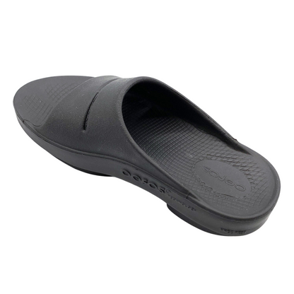 A left angle view of a black foam slide with two over-foot straps and a grippy sole.